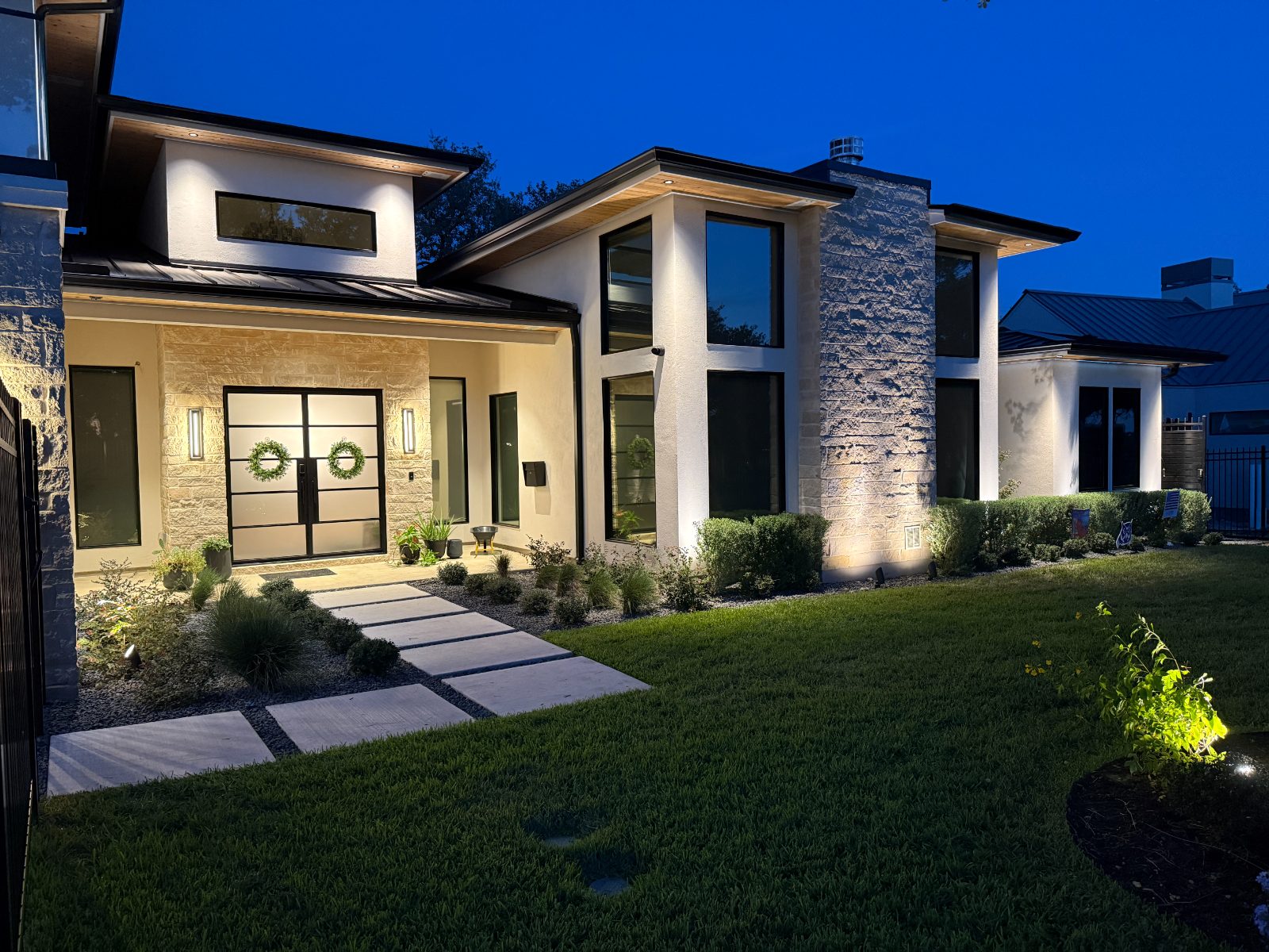 Modern stone home at blue hour with warm-white facade lighting.
